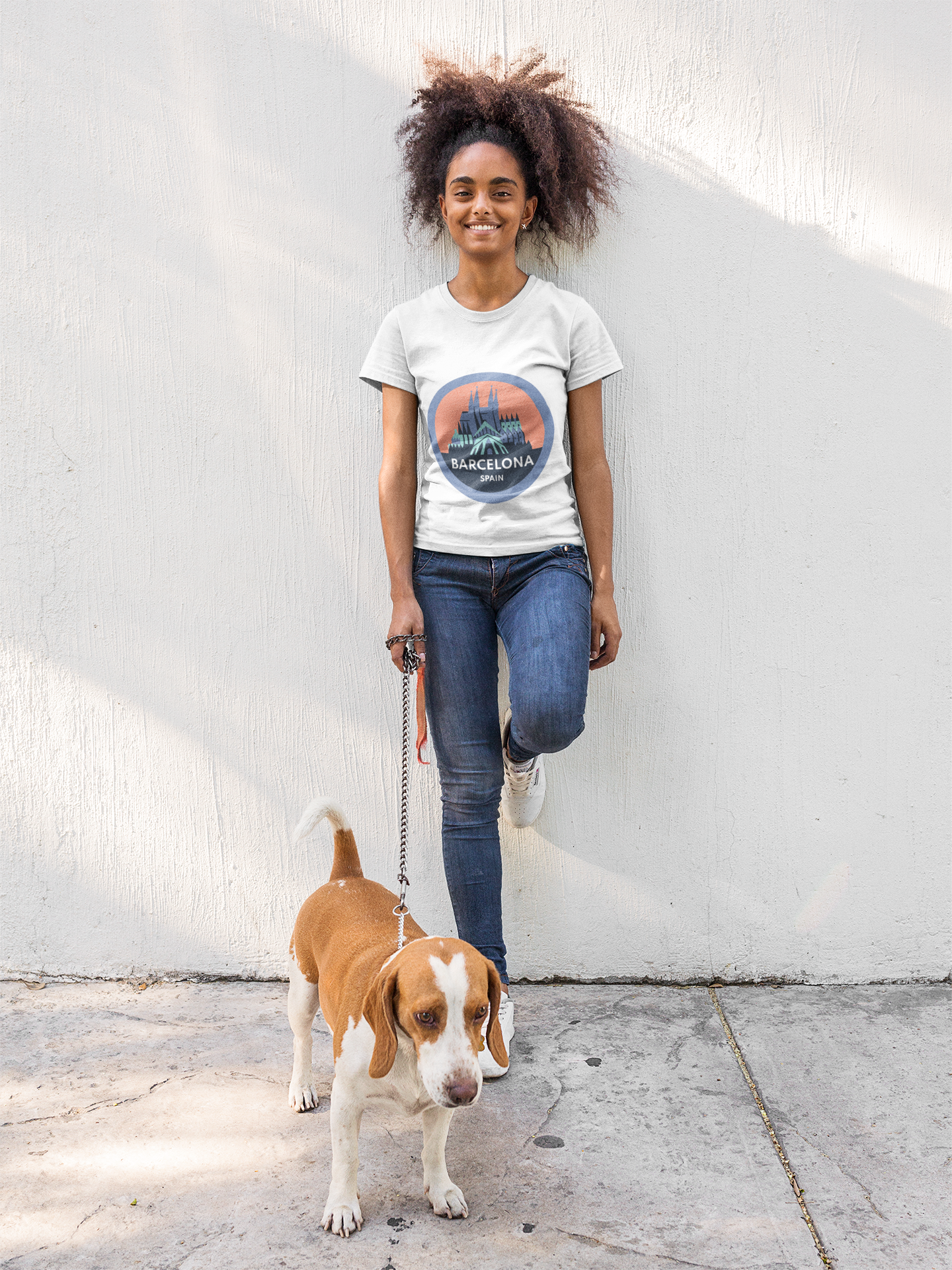 Woman in Nexo Alegre Barcelona T-shirt is walking a dog on a leash against a white wall